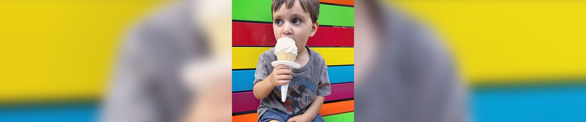 A little boy sitting on the ground eating an ice cream cone.